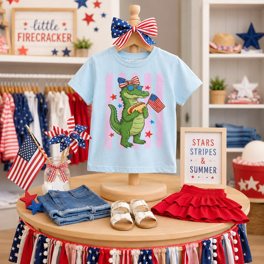 Tea Shirt Shoppe Wholesale light blue 100% cotton youth graphic tee with a green alligator holding a hot dog and an American flag.