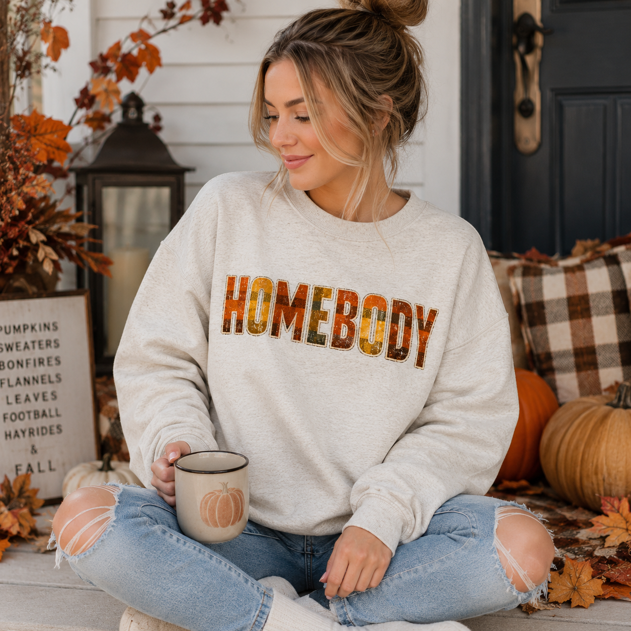Tea Shirt Shoppe Wholesale oatmeal heather crewneck sweatshirt with HOMEBODY plaid graphic worn by a woman on a porch