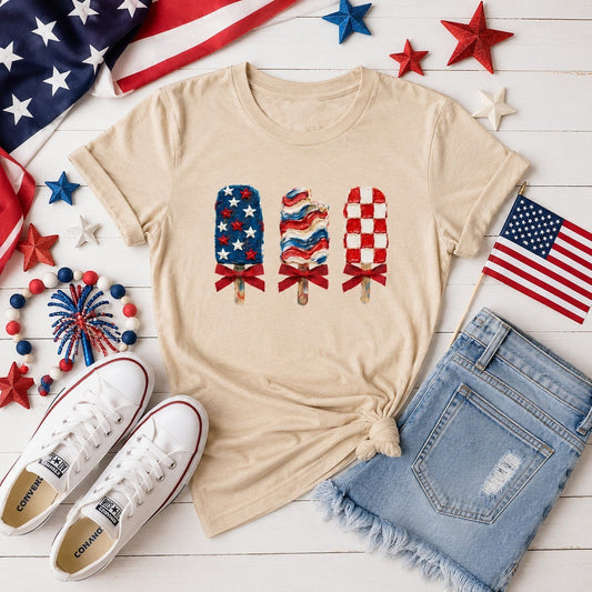 Tea Shirt Shoppe Wholesale beige graphic tee with three patriotic popsicles featuring stars, stripes, and checkerboard patterns.