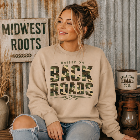 Tea Shirt Shoppe Wholesale sand crewneck sweatshirt with camo Raised On Back Roads graphic worn by a woman