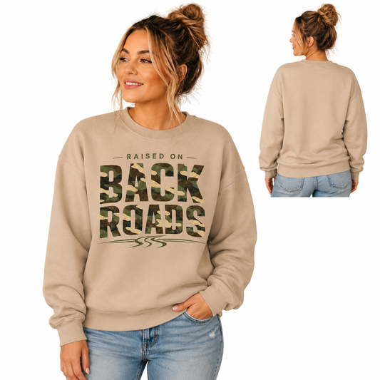 Tea Shirt Shoppe Wholesale sand crewneck sweatshirt with camo Raised On Back Roads graphic worn by a woman