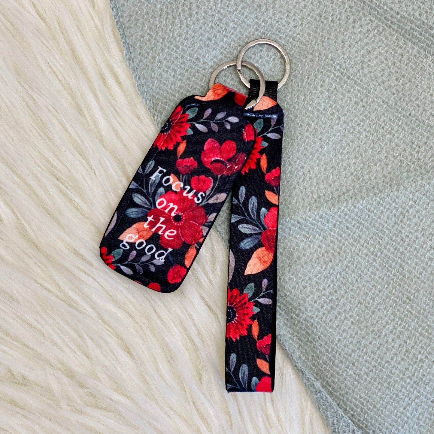 Focus on the Good Lipbalm Holder & Keychain Our floral print Lipbalm Holder & Keychain is not just a cute gift for her, it is also practical. It has a lipbalm holder and a keychain so you can attach it to your purse, backpack or keys, and then you never have to worry about misplacing it. The floral print lipbalm holder is the perfect stocking stuffer for women of all ages.  Red/black Floral  Keychain measurements: 5" Lipbalm holder measurements: 3.75"x1.5"