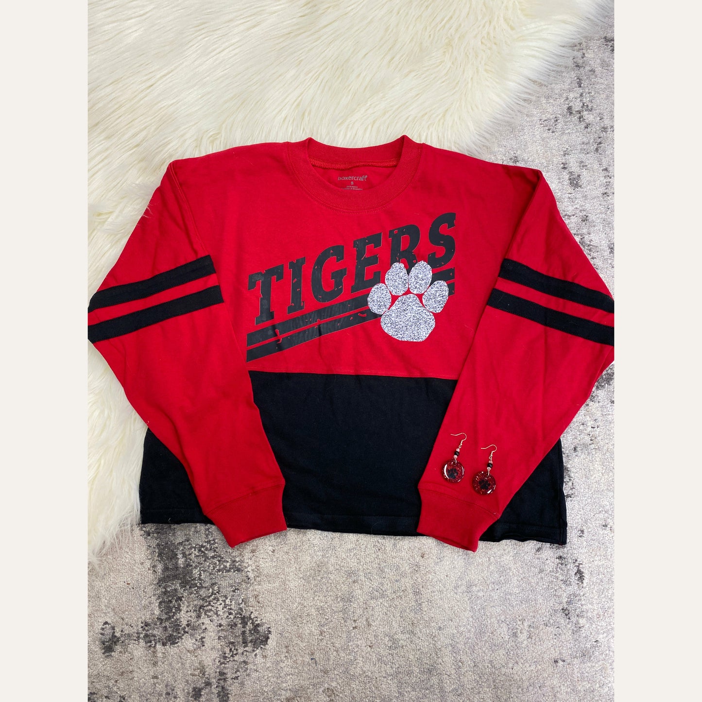 Tigers Long Sleeved Retro Crop ﻿This gorgeous crop is just what you need! The sleeves and top of the crop are red and the bottom half is black. It comes complete with two black stripes on each arm and a tigers logo with a siler sparkly tiger paw. A definite must-have for this football season!  %100 Cotton Machine Washable  Tea Shirt Shoppe 417-262-8828