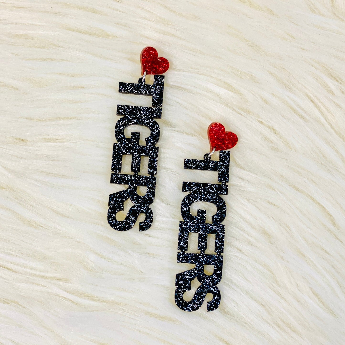 I Love Tigers Earrings You know you want to go all out for your Tigers team! Head to toe showing your pride for them. And these earrings are just the touch you're looking for. You're going to stand out wearing these cuties. At the top is a sparkly red heart and the word Tigers going down vertically in black sparkly letters. They are 3.25" in length and 0.75" wide. 